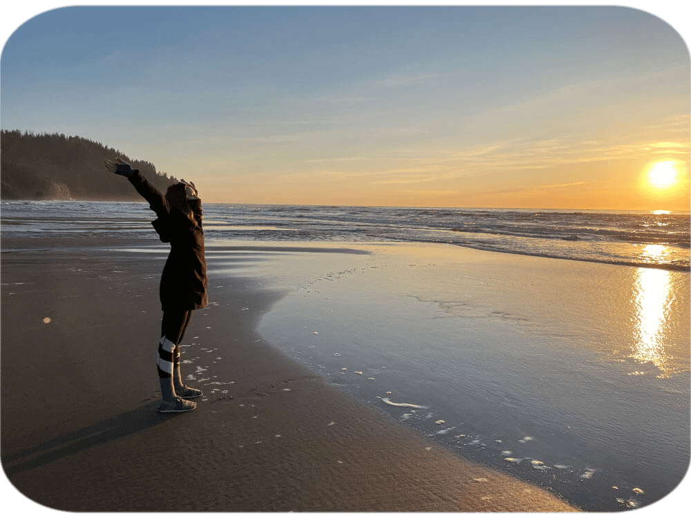 Person with arms raised on beach at sunset